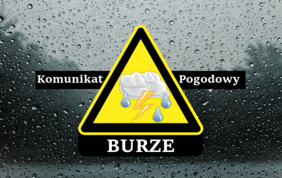 Znak ostrzegawczy z napisem „komunikat pogodowy – burze” na czarnym pasku. W tle szyba pokryta kroplami deszczu. 