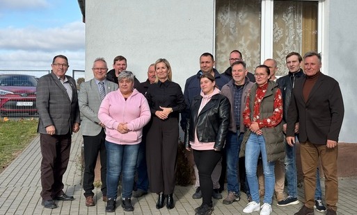 Uczestnicy uroczystości podpisania umów na przebudowę świetlicy wiejskiej w Dębinach pozują do wspólnego zdjęcia przed budynkiem.